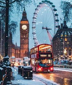 a red double decker bus driving down a street next to a clock tower in the snow