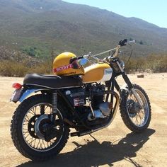 a yellow and black motorcycle parked on top of a dirt field next to a mountain