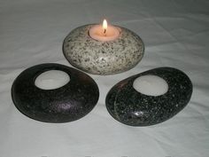 three black and white rocks sitting next to a lit candle on top of a sheet