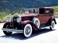 an antique car is parked on the side of the road with mountains in the background