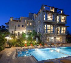 an outdoor swimming pool surrounded by lounge chairs and trees at night with lights on the windows