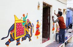 a man painting the side of a building with an elephant on it's side