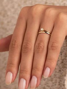 a woman's hand wearing a gold ring with a diamond on it and white nails