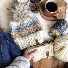 a woman is sitting on the floor with her knitted hat and mitts next to some yarn balls