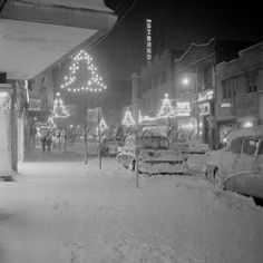 cars parked on the side of a road covered in snow at night with christmas lights