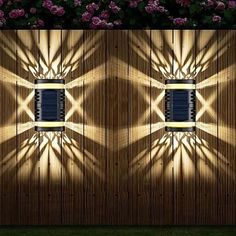 a wooden fence with two lights on it and some pink flowers in the back ground