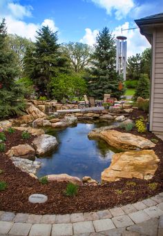 a small pond in the middle of a garden with rocks and gravel around it, surrounded by trees