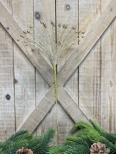 pine cones and greenery are arranged in front of a wooden wall with the letter x on it