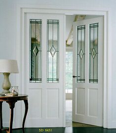 two white doors with stained glass panels in a room next to a table and lamp