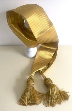 a gold scarf with tassels is on a white table next to a vase