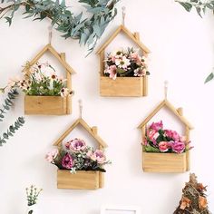 three wooden birdhouses with flowers in them hanging on a wall next to a potted plant