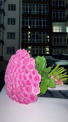 a bouquet of pink roses sitting on top of a white table in front of a tall building