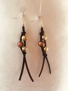 two pairs of black leather earrings with gold and brown beads on them, hanging from hooks