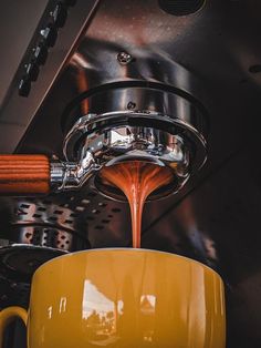 a yellow coffee cup is being filled with liquid from a faucet over a stove