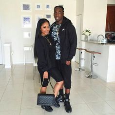 a man standing next to a woman in a kitchen holding a purse and posing for the camera