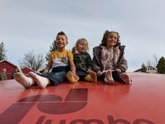 three children sitting on top of a large red object with the word zumbo written on it