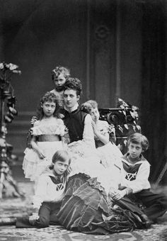 an old black and white photo of people in formal dress sitting on the ground with their children