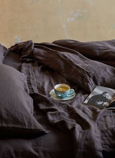 an open book and cup of coffee sit on a bed with brown linens in front of a wall