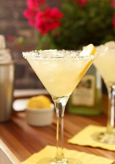 two glasses filled with lemonade sitting on top of a wooden table next to flowers