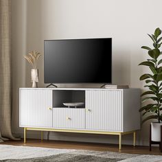 a flat screen tv sitting on top of a white cabinet next to a potted plant