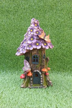 a fairy house with purple flowers and butterflies on it's roof, sitting in the grass