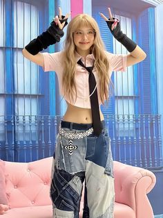 a young woman wearing jeans and a tie standing in front of a pink couch with her hands behind her head