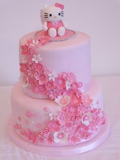 a hello kitty cake with pink and white flowers on the bottom tier, sitting on top of a table