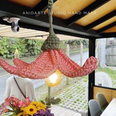 a pink crocheted light hanging from a ceiling in front of a dining room table