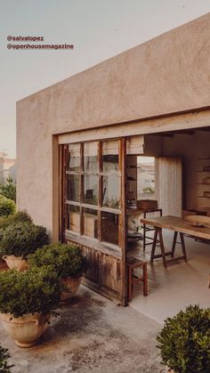 an outdoor dining area with potted plants and wooden table in front of the building