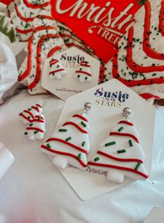 three christmas tree shaped earrings on top of a white table with red and green decorations