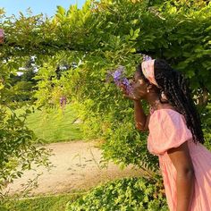 a woman in a pink dress standing under a tree with purple flowers on it's branches