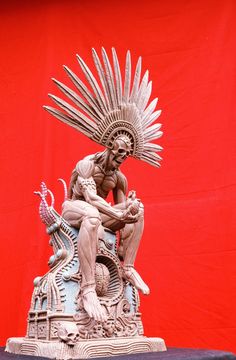 a statue of a man sitting on top of a table next to a red wall