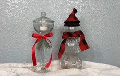 two clear glass candlesticks with red and black bows on them sitting on snow