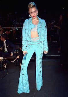 a woman standing in front of a crowd wearing blue pants and a cropped top