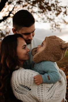 a man and woman are holding a baby in their arms while the child is wearing a teddy bear hat