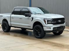 a white pickup truck parked in front of a metal building with black rims and tires