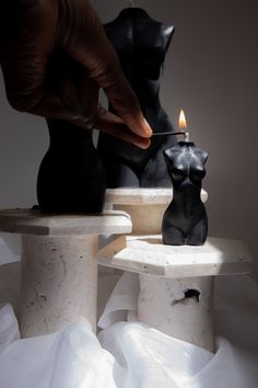 a person lighting a candle on top of two small stools in the shape of cats