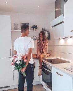 a man and woman standing in a kitchen next to an oven with flowers on the counter