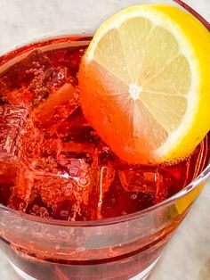 a close up of a drink in a glass with ice and lemon on the side