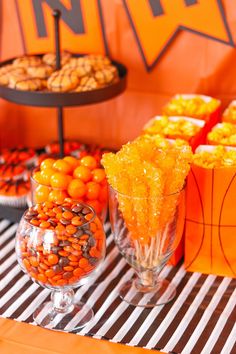 an orange and black basketball themed dessert table with candy in glass vases on top