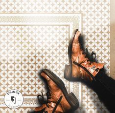 a pair of brown boots sitting on top of a tiled floor next to a person's legs