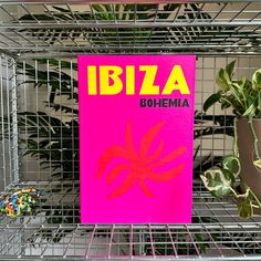 a pink book sitting on top of a metal shelf next to a potted plant