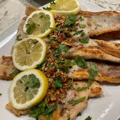 fish with lemons, nuts and herbs on a white plate