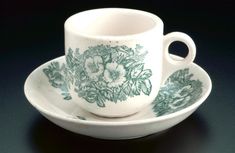 a cup and saucer with flowers painted on the side sitting on a black surface