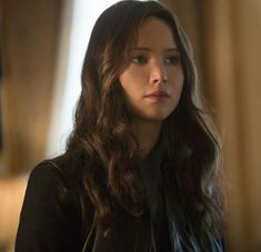 a woman with long brown hair wearing a black shirt and leather jacket looking off into the distance