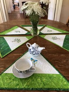 a table topped with plates and cups on top of a wooden table next to a vase filled with flowers