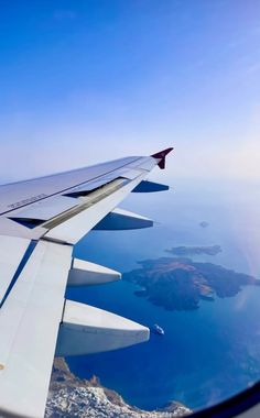 the wing of an airplane as it flies over some blue water and land in the background