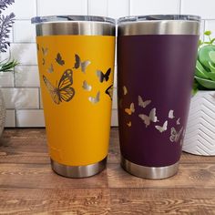 two colorful tumblers sitting on top of a wooden table next to a potted plant