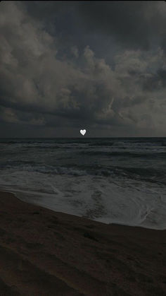 a heart shaped object floating in the air on top of a beach next to the ocean