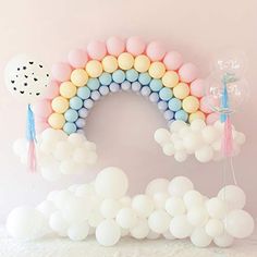 a rainbow balloon arch with pastel colors and tassels on the top is surrounded by balloons